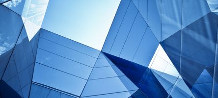 This is a photo of the glass façade of a building taken from a low angle. The triangular and square shapes of the windows appear abstract.