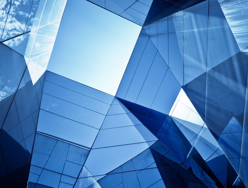 Foto einer Glasfassade eines Gebäudes aus der Froschperspektive. Die dreieckigen und quadratischen Formen der Fenster wirken abstrakt.