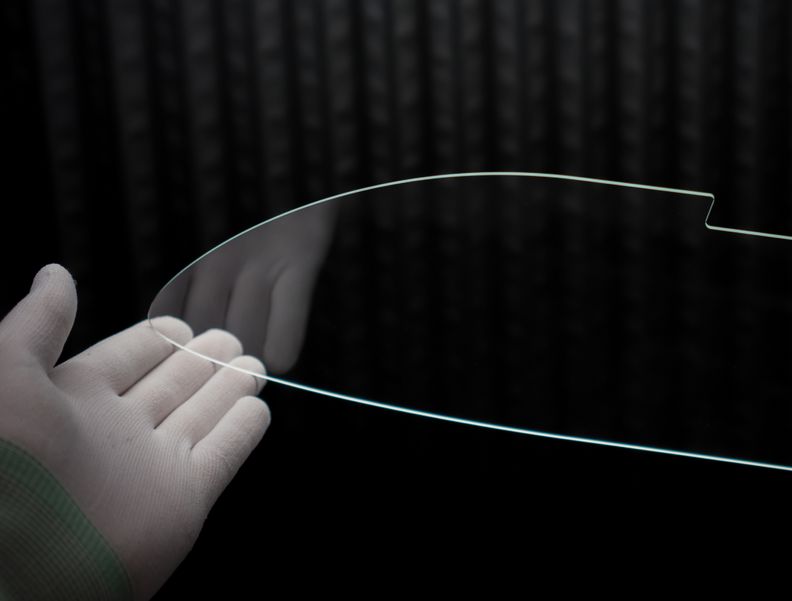 Das Foto zeigt, wie eine Glasprobe mit zwei Händen in weißen Handschuhen gehalten wird.