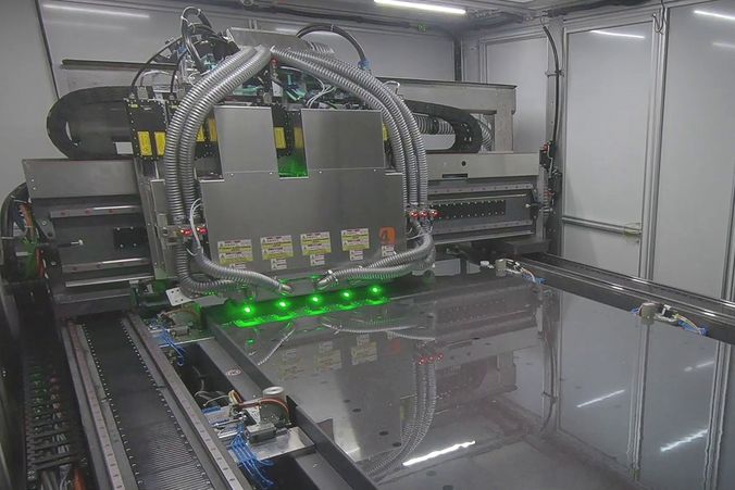 Das Bild zeigt das Innere einer Laseranlage zur Glasstrukturierung. Mehrere Laserstrahlen werden über das Substrat geführt.