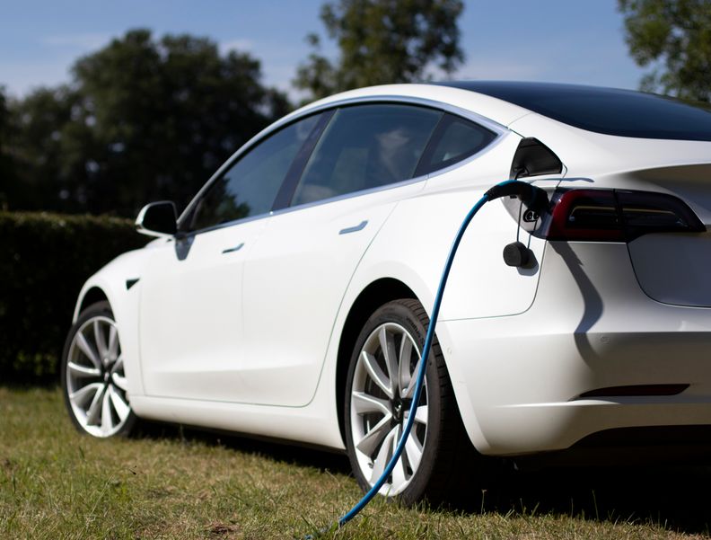 Photo of a white electric car being charged with a cable.