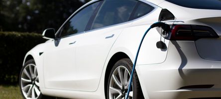 Photo of a white electric car being charged with a cable.