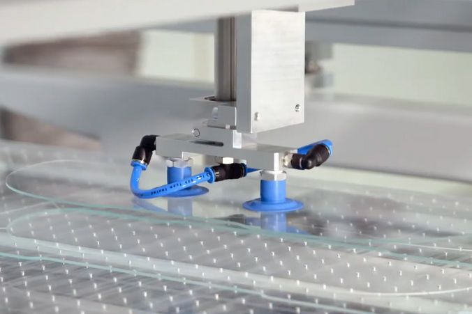 Foto eines Roboterarms mit Vakuumsauger, der ein geschnittenes Glasteil transportiert.