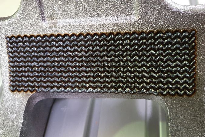 Nahaufnahme einer laserstrukturierten Oberfläche. Man sieht eine gleichmäßige Musterung auf der metallischen Oberfläche.