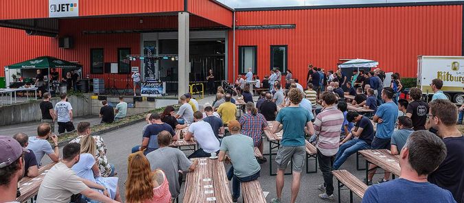 Viele Gäste sitzen bei der Eröffnungsfeier vor der neuen, roten Montagehalle.