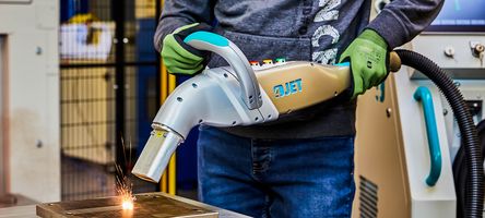 Ein 4JET Mitarbeiter hält das Handstück des JETLASER M100 und reinigt damit eine metallische Oberfläche.