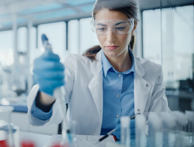 Eine Laborassistentin pipettiert flüssige Substanzen mit einer Glaspipette.