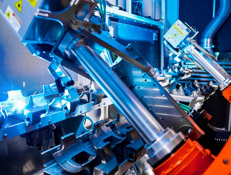 Nahaufnahme von zwei Roboterarme mit jeweils einem Laserprozesskopf, die eine Struktur in Bauteile einbringen.