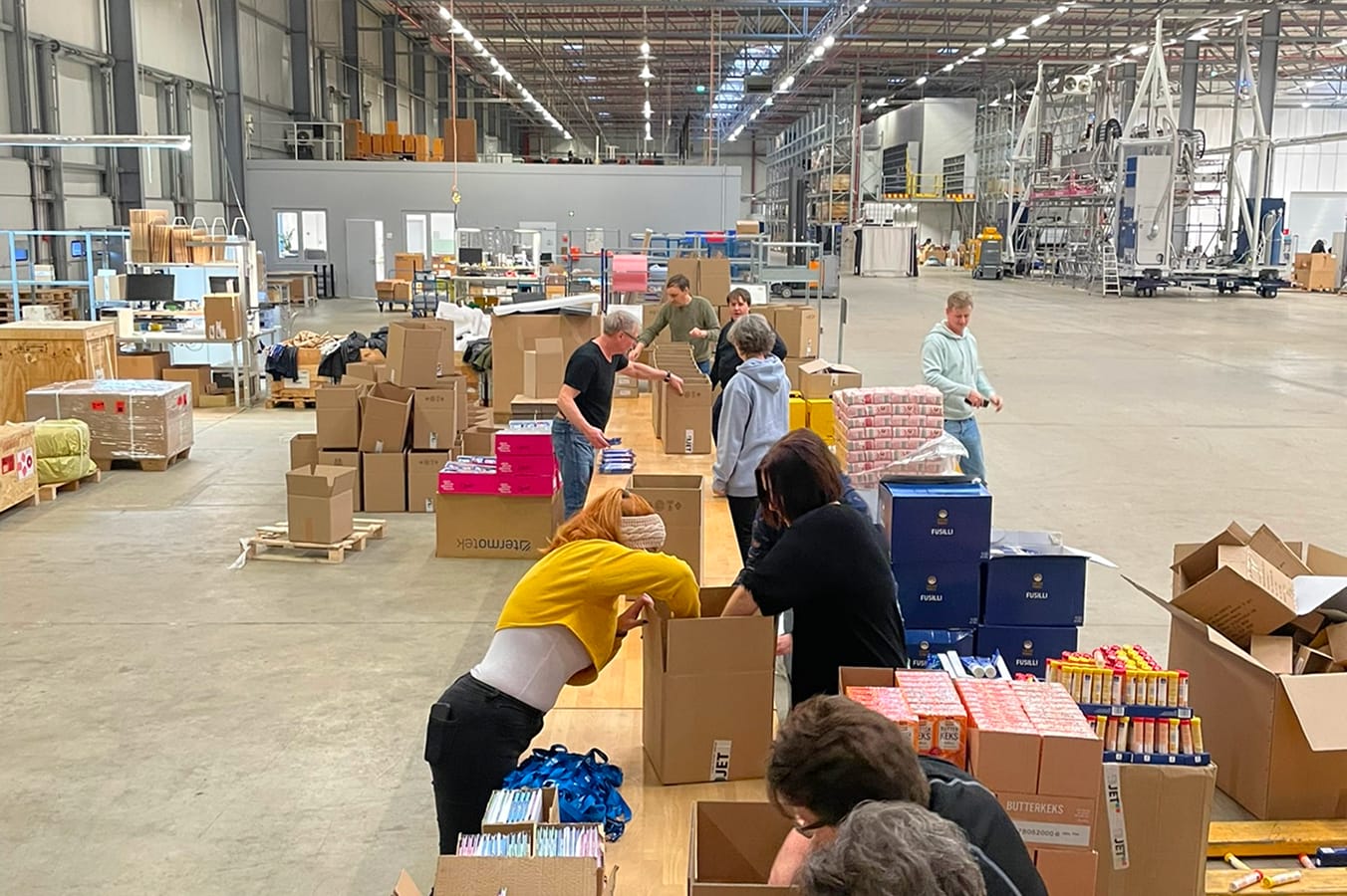 An einem langen Tisch packen mehrere 4JET Mitarbeiter Spendenpakete.