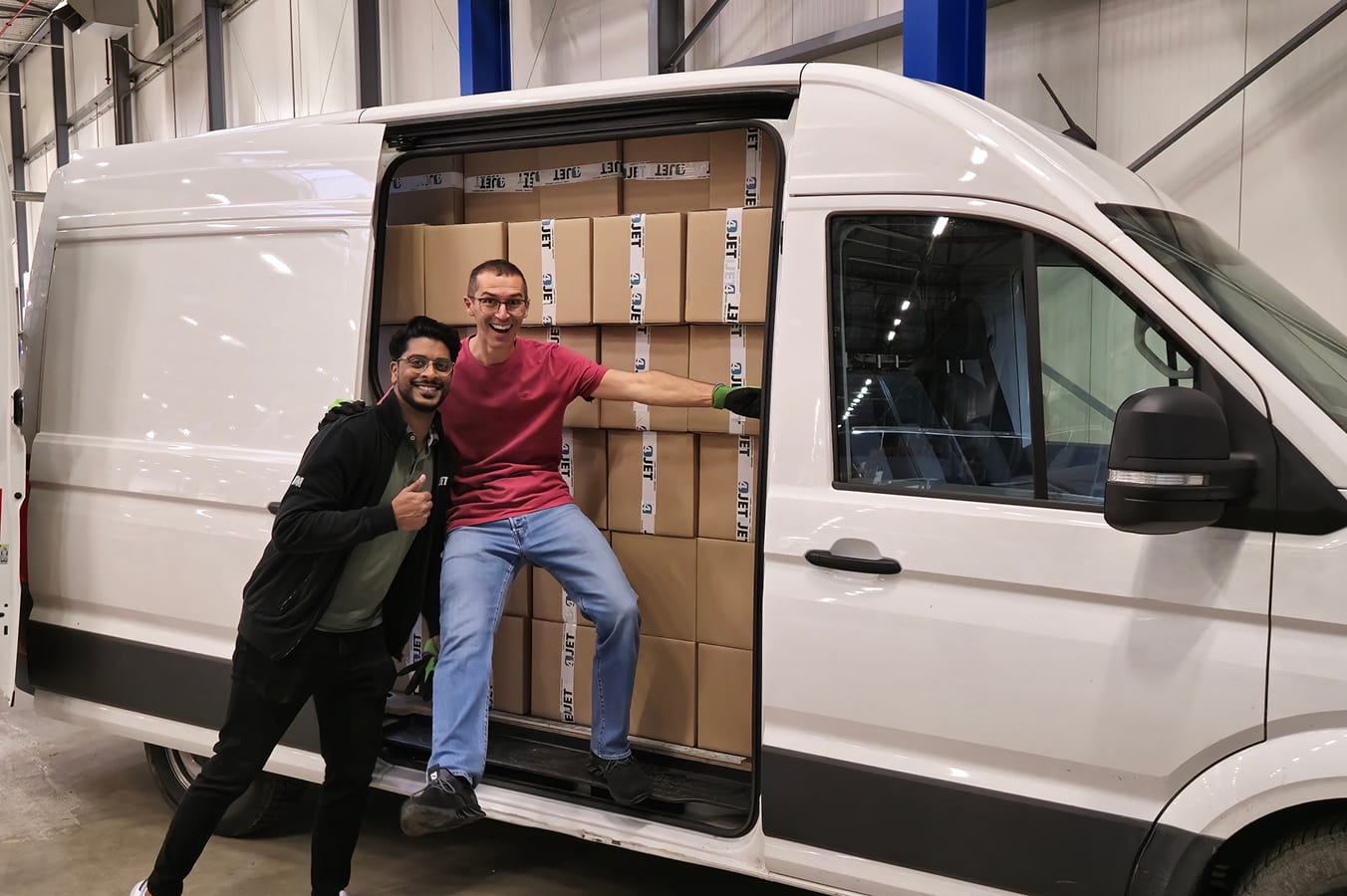 Ein weißer Transporter ist beladen mit gepackten Kartons. Zwei 4JET-Mitarbeiter posieren glücklich vor dem Fahrzeug.
