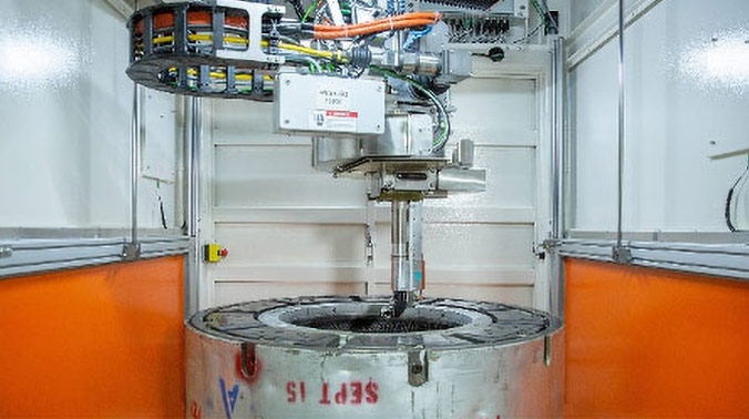 Auf dem Bild ist das Innere des Systems zu sehen. Ein 6-Achsen Reinigungskopf, der die Bearbeitung von komplizierten Formgeometrien ermöglicht, ist über der Reifenform positioniert.