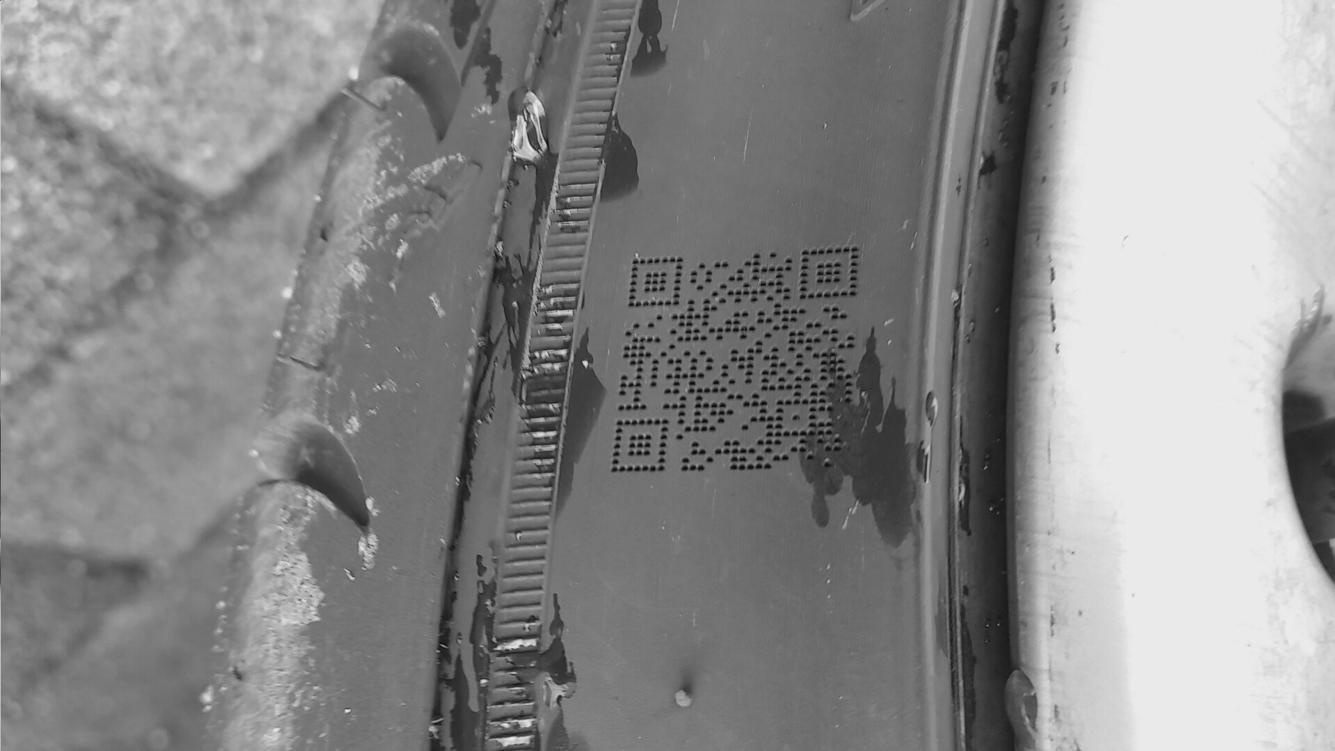 Ein QR-Code auf einer verschmutzten Reifenseitenwand; rund um den Code sind Schmutz, Abrieb und Gebrauchsspuren zu erkennen.