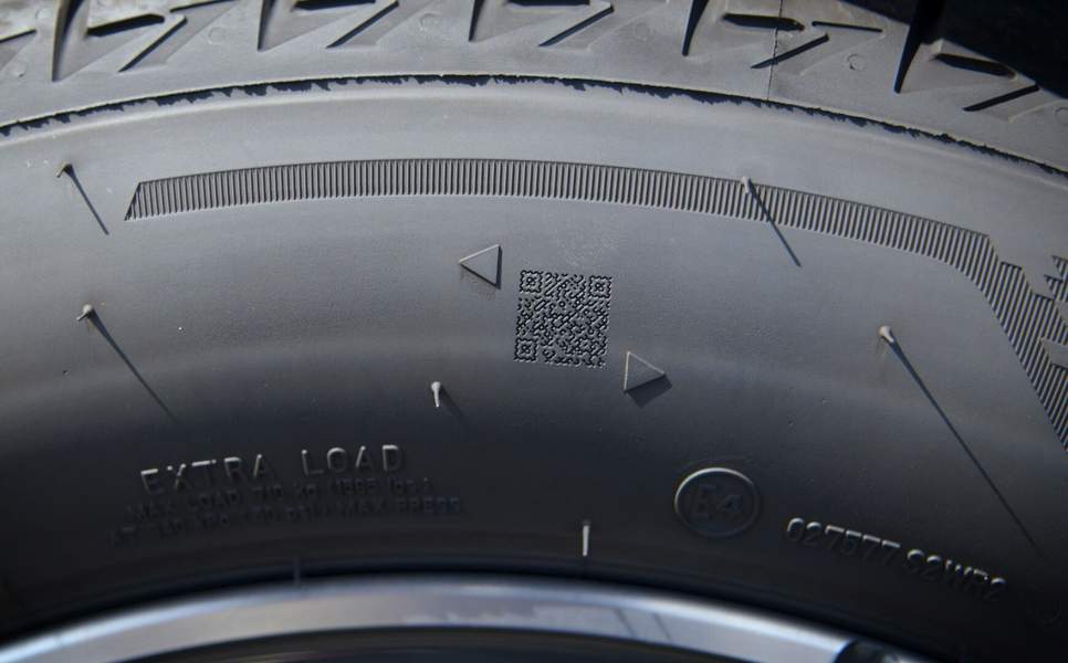 Ein auf eine Reifenseitenwand gravierter QR-Code zwischen zwei dreieckigen Fiducial-Markern, neben weiteren Seitenwandkennzeichnungen.