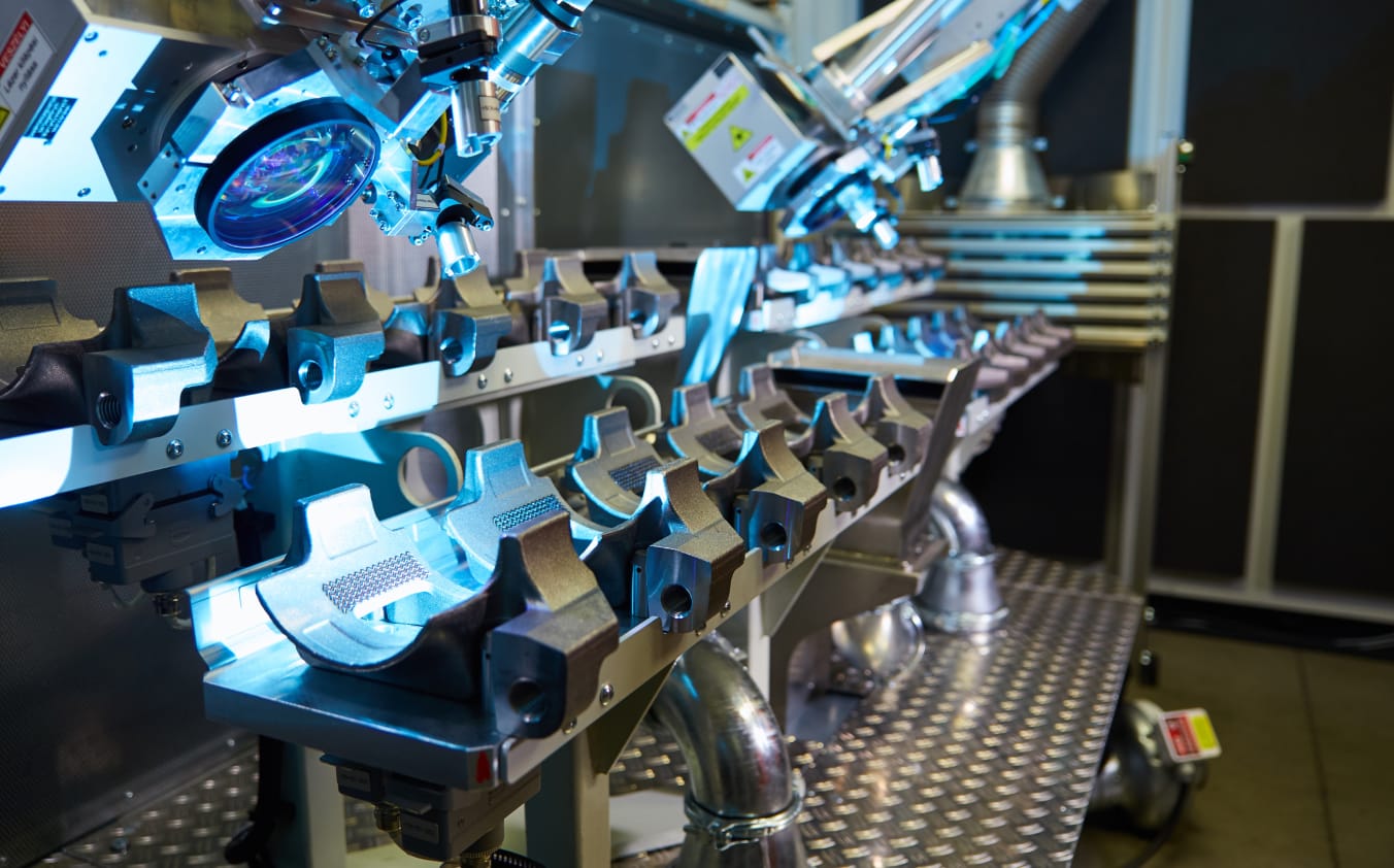 Zwei Laserprozessköpfe bearbeiten mehrere metallische Bauteile.