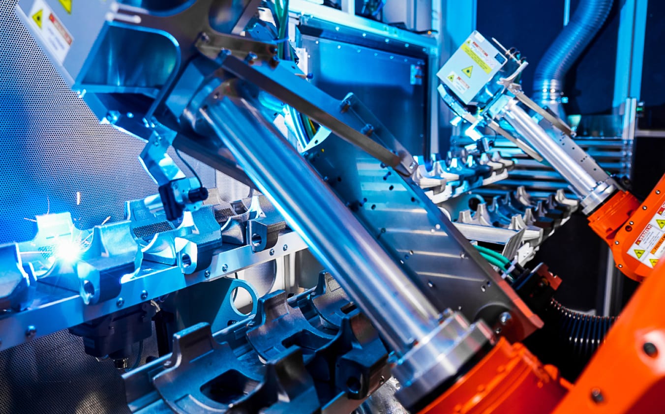 An einem Roboterarm befindet sich ein Laserprozesskopf, der Bauteile mit einem hellen Laserstrahl reinigt.