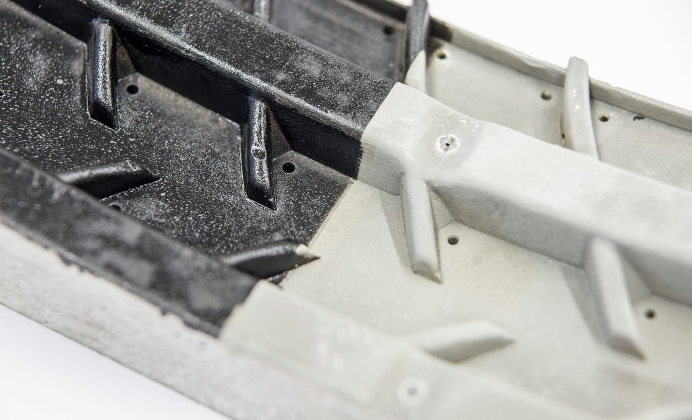 Ein Abschnitt einer Reifenform wurde bis zur Hälfte gereinigt. Links ist die Reifenform von einer grauen Schmutzschicht überzogen, rechts ist die helle, gereinigte Oberfläche zu sehen.