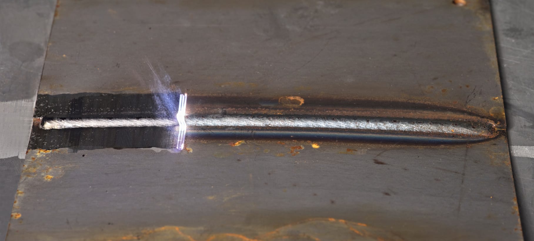 Auf einer Metallplatte befindet sich eine längliche Schweißnarbe, die von einen Laserstrahl gereinigt wird.