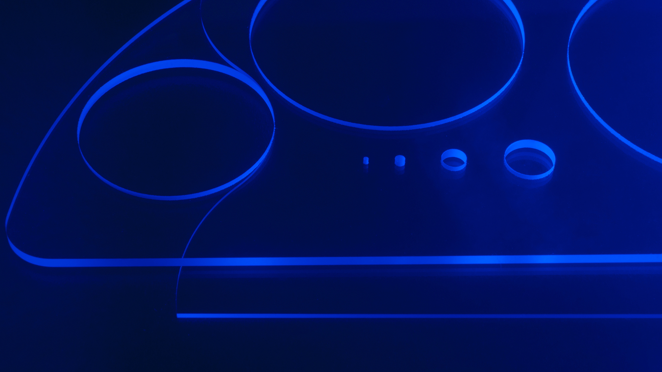 Blau beleuchtete freiförmige Glasscheibe mit gebohrtem Löchern verschiedener Durchmesser.