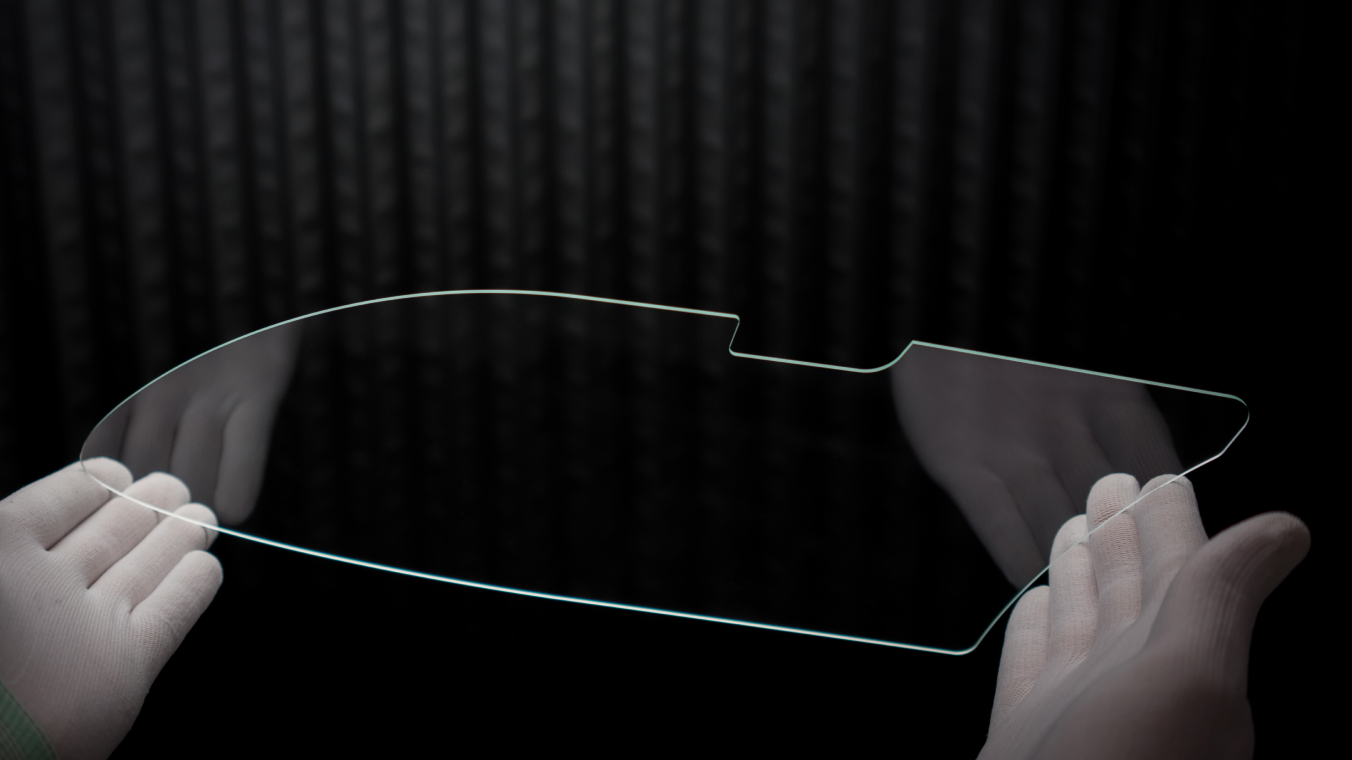 Laser-cut freeform glass component. The component is held by two gloved hands.