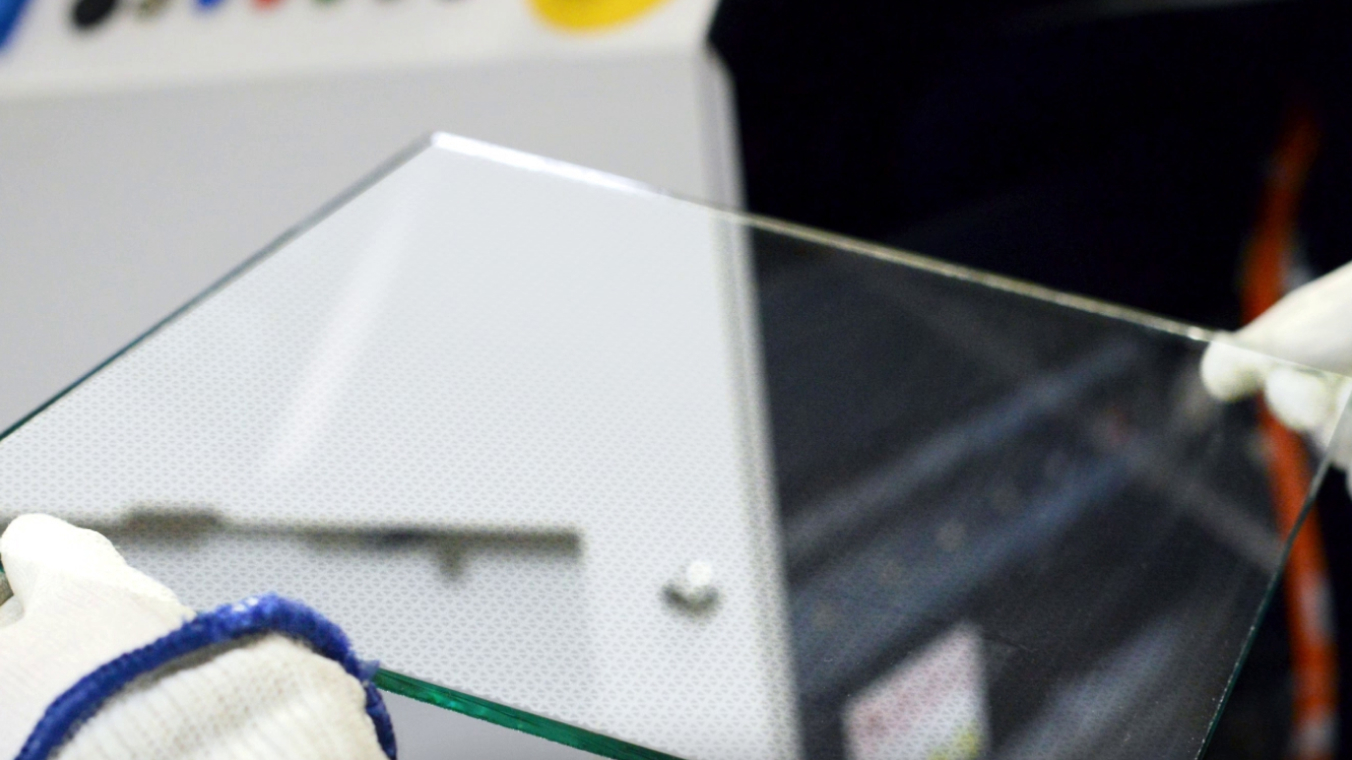 Glasscheibe mit fein strukturiertem Muster. Die Scheibe wird von zwei Händen mit Handschuhen gehalten.