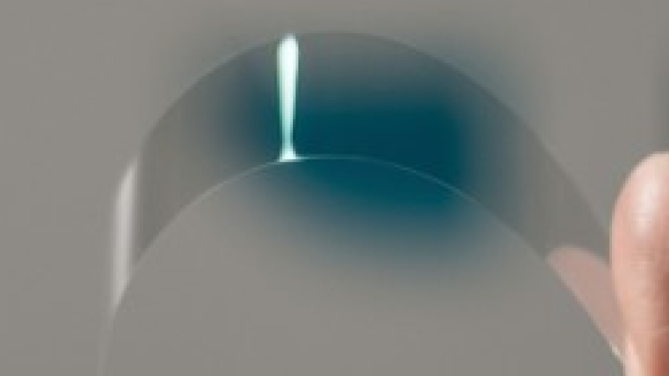 Streifen aus ultradünnem Glas. Der Streifen wird zwischen zwei Fingern in einem engen Radius gebogen.