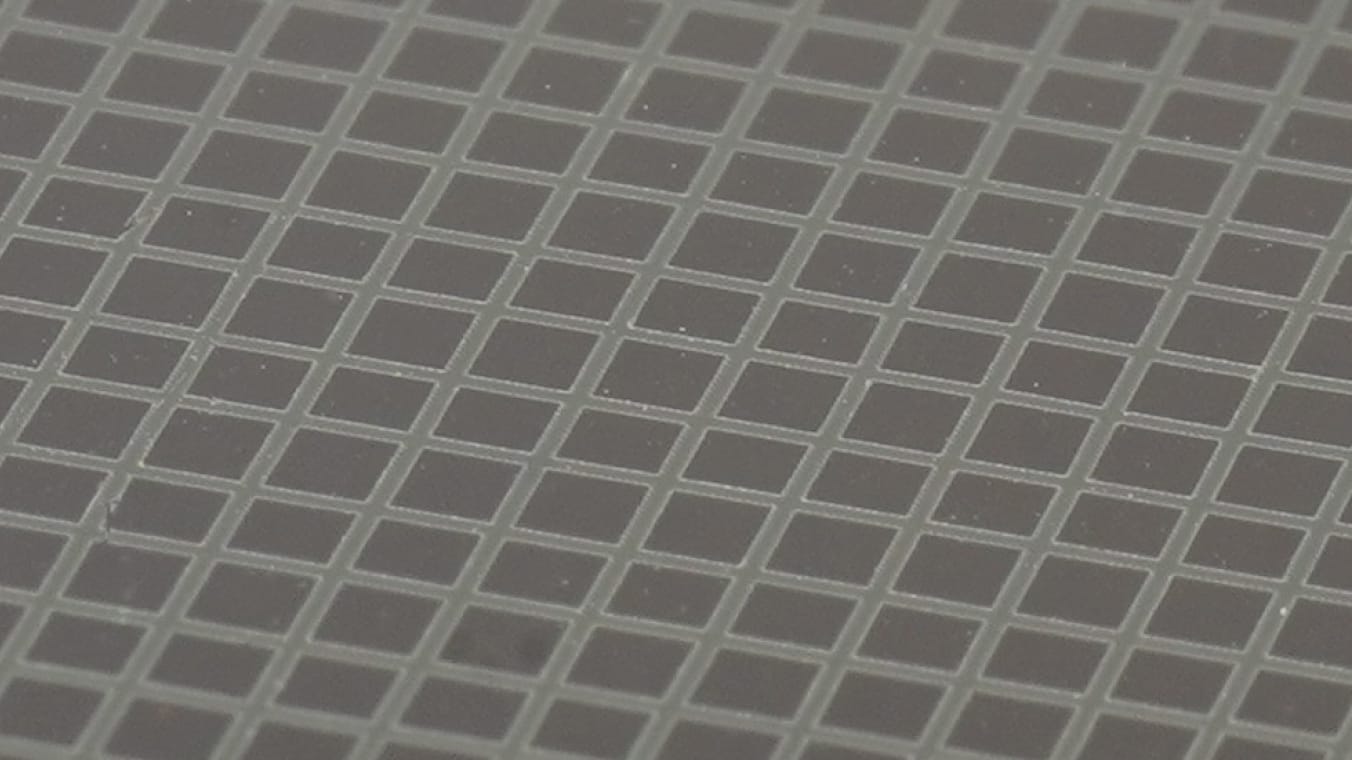 Makroaufnahme eines gitterförmigen Abtragsmuster. Die Abtragslinien sind dabei heller als die unbearbeiteten Bereiche des Materials.