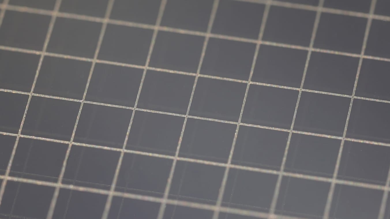 Scheibe mit gitterförmigen Abtragsmuster. Die Abtragslinien heben sich hell vom unbearbeiteten Material ab.