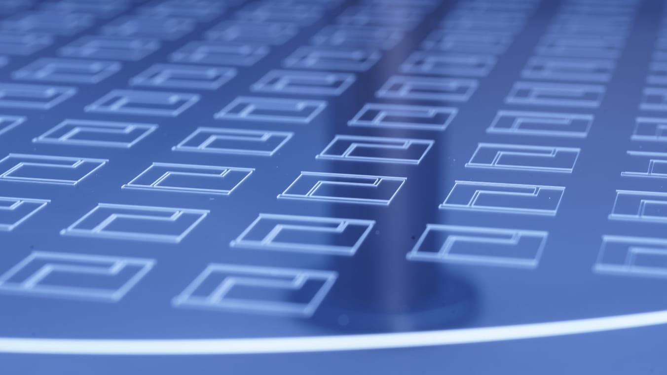 Blau beleuchteter Glaswafer. Auf dem Wafer ist ein regelmäßiges Muster mit feinen Linien aufgebracht.